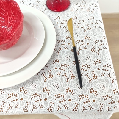 Mesa posta com toalha branca rendada, prato branco, taça vermelha, cacho de uvas e faca com cabo preto e lâmina dourada.