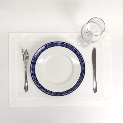 Mesa posta com prato de borda azul, talheres prateados, copo de vidro e toalhete branco