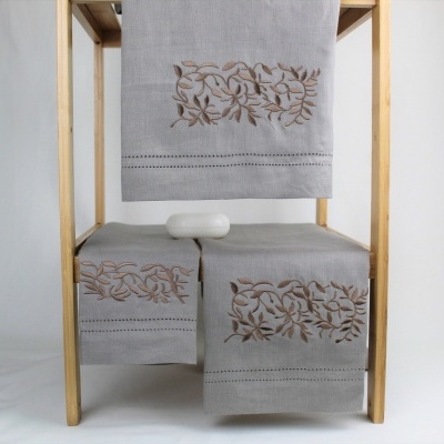 Três toalhas cinza com bordados florais castanhos numa estrutura de madeira clara