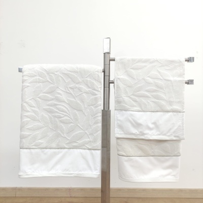 Toalhas brancas com padrão de folhas em relevo penduradas num suporte metálico