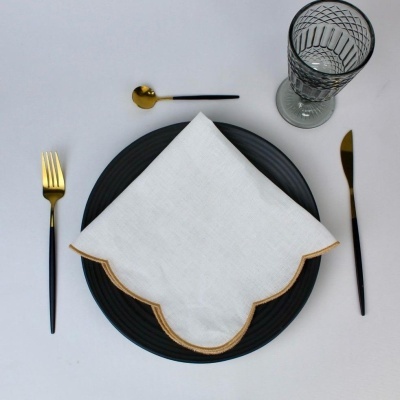 Mesa posta com talheres dourados e pretos, prato preto, guardanapo branco com borda dourada e copo de vidro decorado