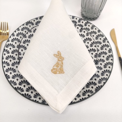 prato com padrão geométrico preto e branco e guardanapo branco bordado com coelho dourado