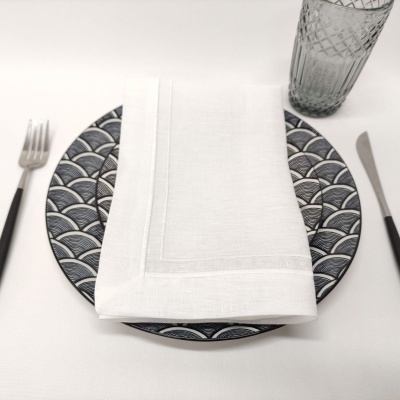 Conjunto de jantar com prato decorativo azul e branco, guardanapo branco, talheres pretos e copo transparente