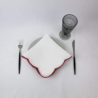 Mesa posta com prato cinzento, guardanapo branco com borda vermelha, talheres preto e copo de vidro