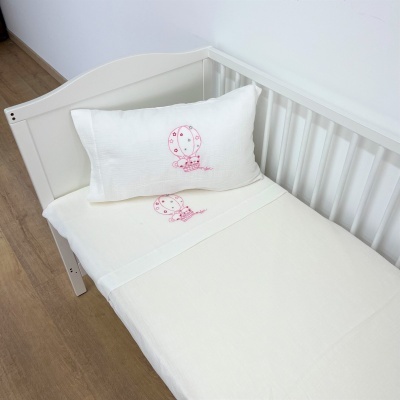 Berço branco com lençol e almofada brancos com desenhos cor-de-rosa