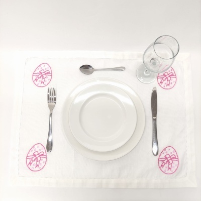 Conjunto de loiça branca com talheres, copo e toalha decorada com ovos de Páscoa rosa