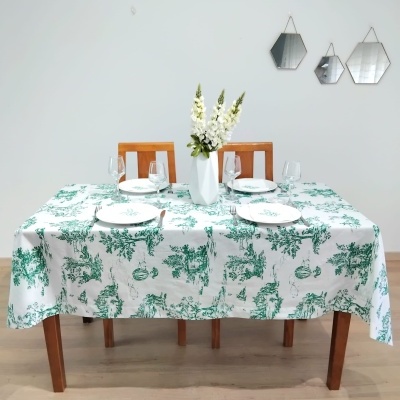 Mesa de madeira com toalha branca com estampado verde e utensílios de jantar