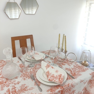 Mesa posta com toalha e napkins vermelhos e brancos, pratos, copos, talheres, garrafa decantadora e castiçais dourados