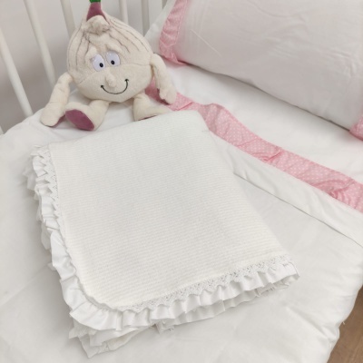 Colcha branca com renda e folho numa cama branca com fronhas brancas com borda rosa e peluche de alho.