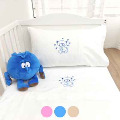 Lençóis brancos para berço com bordado azul de urso e peluche azul num berço branco