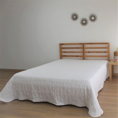 Cama de madeira com colcha branca e decoração simples