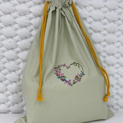 Saco de tecido verde claro com cordão amarelo e desenho de coração floral