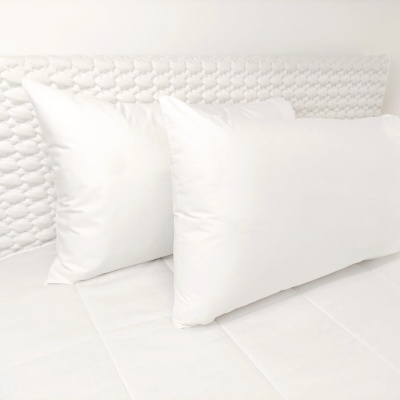 Almofadas brancas numa cama com cabeceira branca texturada