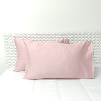 Duas almofadas cor-de-rosa numa cama com cabeceira branca texturizada