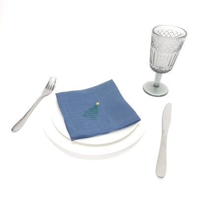 Conjunto de loiça com prato branco, guardanapo azul com árvore de Natal, talheres e copo de vidro