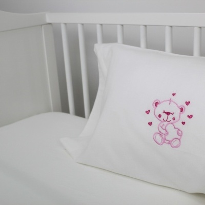 Travesseiro branco com ursinho rosa bordado no berço branco
