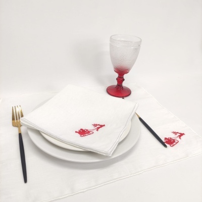 Conjunto de mesa com prato branco, talheres pretos e dourados, guardanapo branco com bordado vermelho e copo com base vermelha.