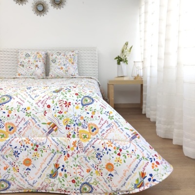 Conjunto de cama branco com padrão colorido floral, pássaros e texto manuscrito, quarto iluminado e minimalista.