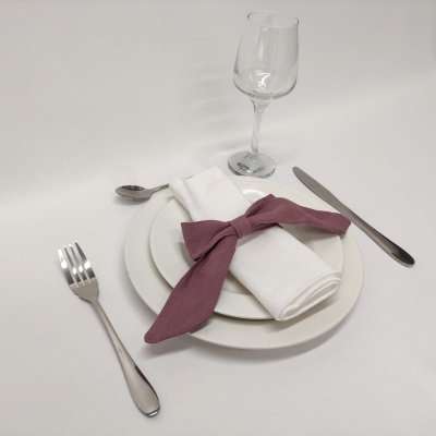 Mesa posta com pratos brancos, guardanapo com laço vinho, talheres e copo