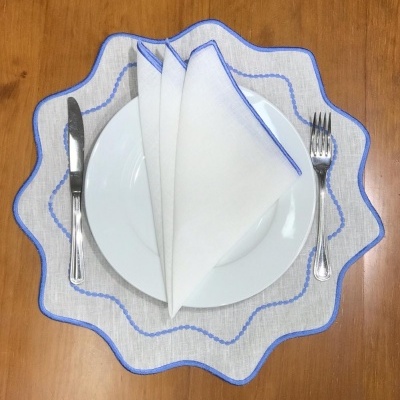 Conjunto de mesa com toalha branca e azul, prato branco, guardanapo branco, faca e garfo numa mesa de madeira