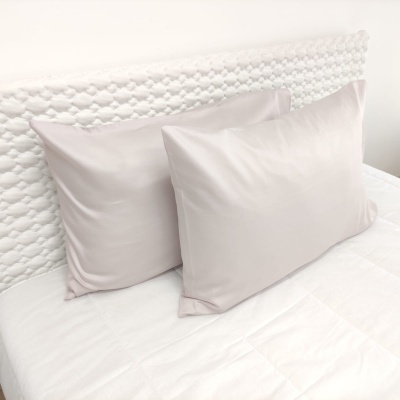 Almofadas creme claro com fronhas lisas sobre cama com cabeceira branca trançada