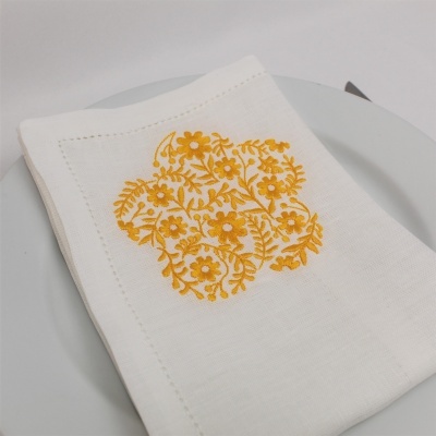 Guardanapo branco com bordado floral amarelo sobre prato branco