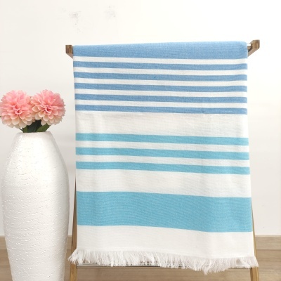 Toalha listrada azul, branca e turquesa pendurada com vaso branco e flores cor de rosa