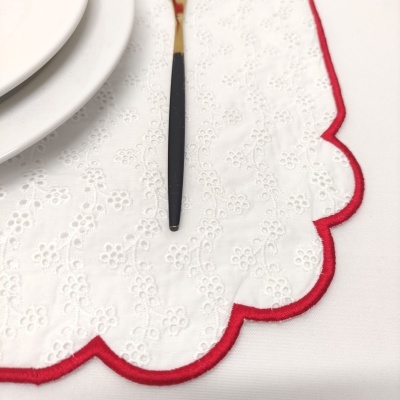 Guardanapo branco bordado com bainha vermelha numa mesa com prato e utensílio.