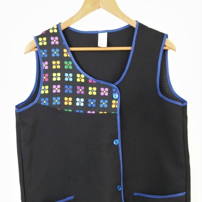 Colete preto com padrão colorido e botões azuis pendurado num cabide de madeira