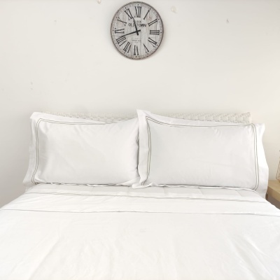 Cama com roupa de cama branca e relógio de parede acima