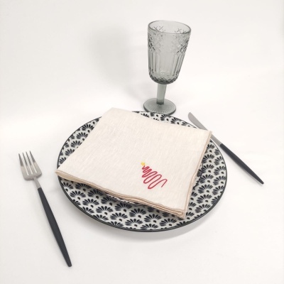 Mesa posta com prato branco e preto, guardanapo branco com desenho, talheres pretos e copo de vidro transparente