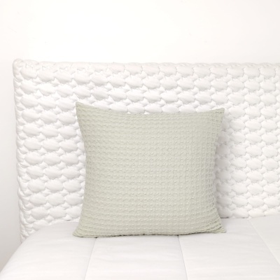 Almofada cinzento claro texturizada em cama branca com cabeceira acolchoada