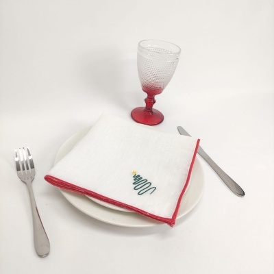 Conjunto de mesa com prato branco, talheres metálicos, guardanapo natalício e copo com base vermelha