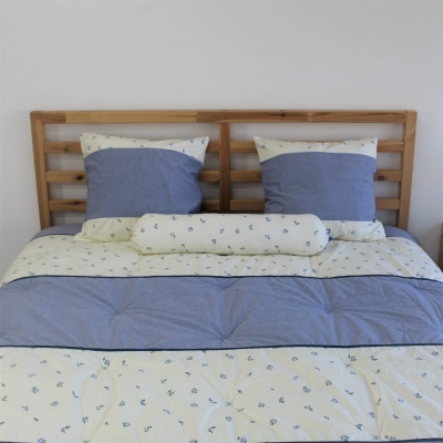 Cama com roupa de cama azul e creme com padrões florais e estrutura de madeira clara