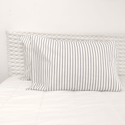 Almofadas brancas com riscas pretas verticais numa cama branca.