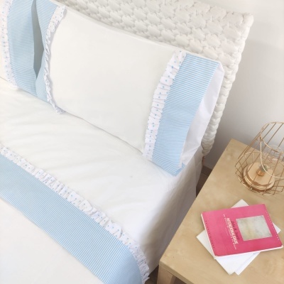 Lençol e almofada brancos com riscas azuis em cama ao lado de mesa de cabeceira