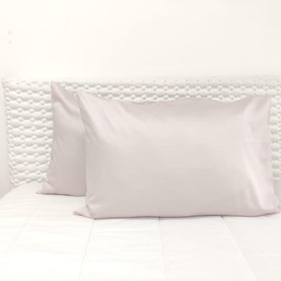 Capa de almofada cinzenta clara em cama branca com cabeceira acolchoada