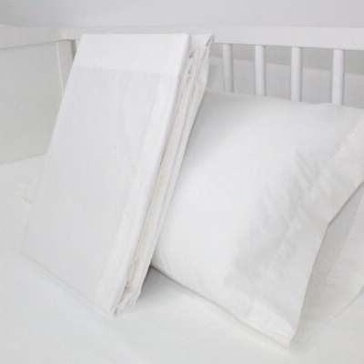 Conjunto de cama branco com almofada e lençol num berço branco