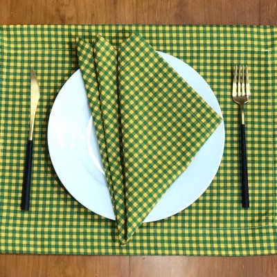 Conjunto de mesa com padrão xadrez amarelo e verde, prato branco, talheres dourados e pretos