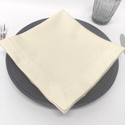 guardanapo branco creme sobre prato cinzento escuro com talheres e copo transparente