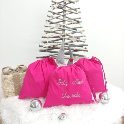 Três sacos rosa com texto de Natal, bolas prateadas, presente e árvore de Natal de galhos rústicos