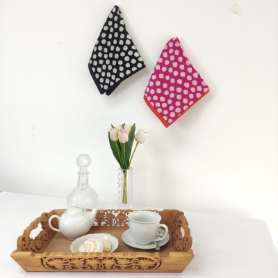 Bandeja de madeira com chávena, bule, bolo, jarro com tulipas e toalhas de bolinhas penduradas na parede
