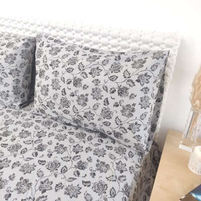 Conjunto de roupa de cama cinzenta com padrão floral e mesa de cabeceira com vaso de plantas secas