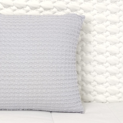 Almofada cinzenta com textura tipo waffle em cama com cabeceira branca acolchoada