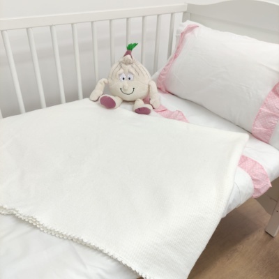 Cama de criança com roupa branca, bordas rosas, manta branca e peluche de cebola