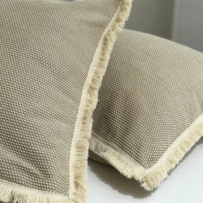 Almofadas bege com franjas brancas em superfície branca