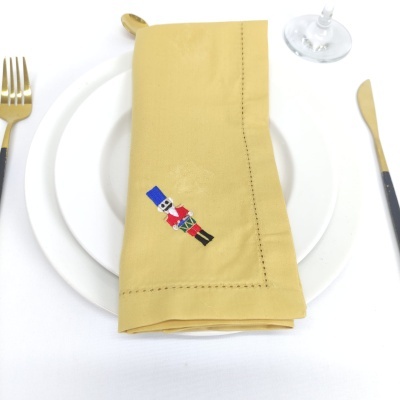 Guardanapo amarelo com bordado de soldado de chumbo em prato branco, com talheres dourados e copo