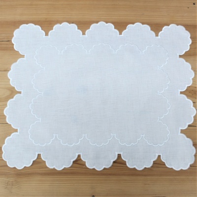 Toalhete branco com padrão bordado e bordas recortadas sobre madeira