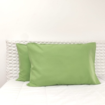 Duas almofadas verdes sobre cama branca com cabeceira acolchoada branca