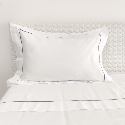 Travesseiro branco com borda preta sobre cama branca com cabeceira texturizada